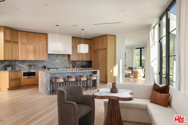 interior space with backsplash, pendant lighting, light hardwood / wood-style flooring, and a center island with sink