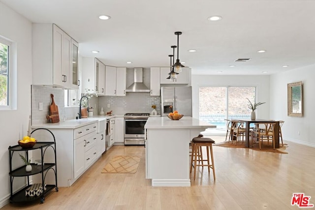 kitchen featuring a wealth of natural light, a center island, wall chimney exhaust hood, and stainless steel appliances