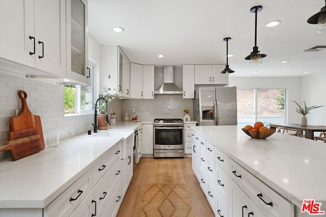 kitchen with wall chimney exhaust hood, a healthy amount of sunlight, white cabinetry, and appliances with stainless steel finishes