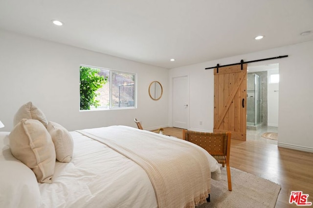 bedroom with ensuite bathroom, a barn door, and light hardwood / wood-style floors