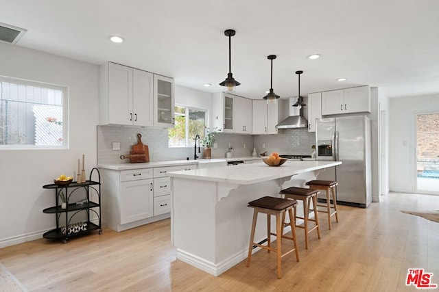 kitchen with stainless steel fridge, light wood-type flooring, a kitchen island, and wall chimney range hood