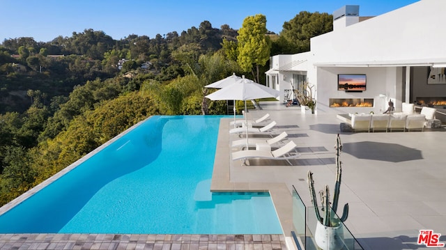 view of pool with an outdoor living space with a fireplace and a patio