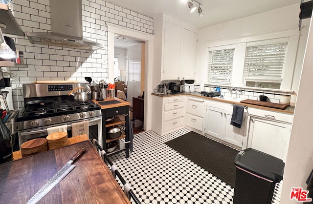 kitchen featuring white cabinets, stainless steel range with gas stovetop, decorative backsplash, and wall chimney range hood