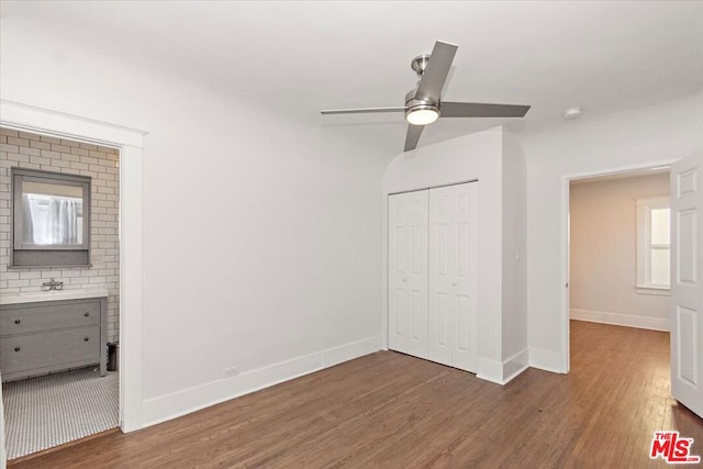 unfurnished bedroom featuring sink, ensuite bath, dark hardwood / wood-style flooring, a closet, and ceiling fan