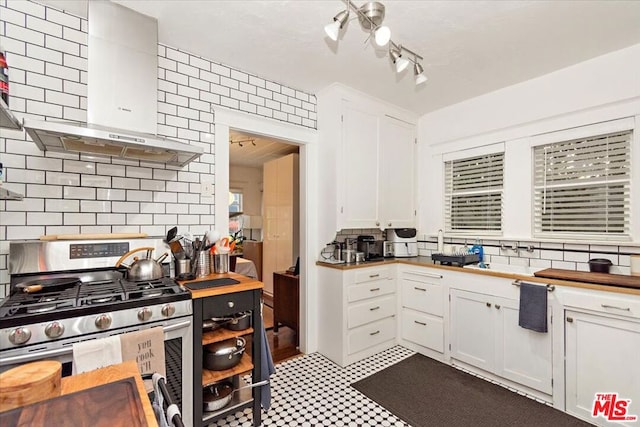 kitchen with stainless steel range with gas cooktop, wall chimney range hood, white cabinets, and decorative backsplash