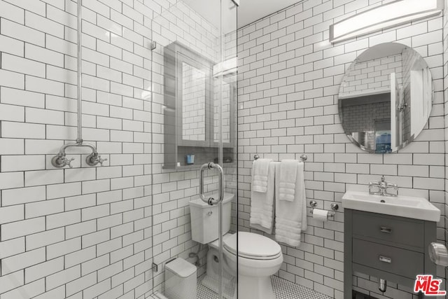 bathroom featuring a shower with door, tile walls, tile patterned flooring, vanity, and toilet