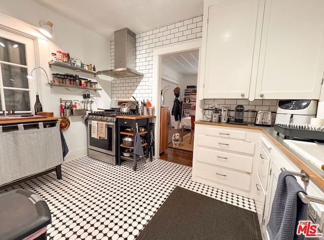 kitchen with sink, stainless steel gas range, white cabinets, decorative backsplash, and wall chimney exhaust hood