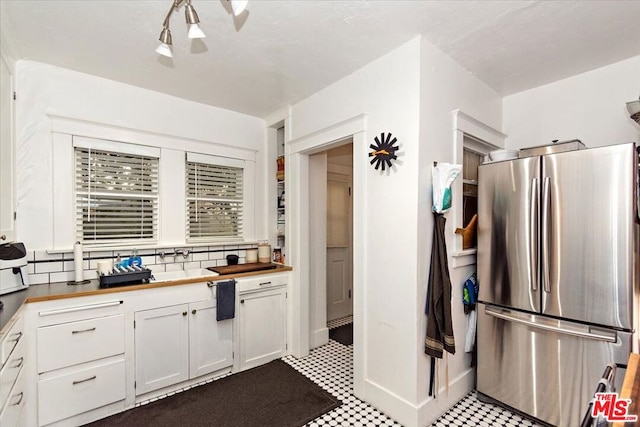 kitchen with white cabinetry, backsplash, and stainless steel refrigerator