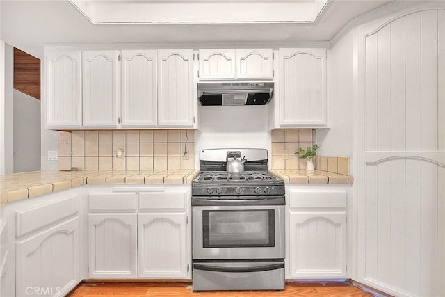 kitchen featuring light wood-type flooring, range hood, white cabinets, stainless steel gas range oven, and decorative backsplash