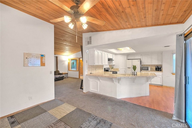 kitchen featuring appliances with stainless steel finishes, white cabinets, a breakfast bar, kitchen peninsula, and lofted ceiling