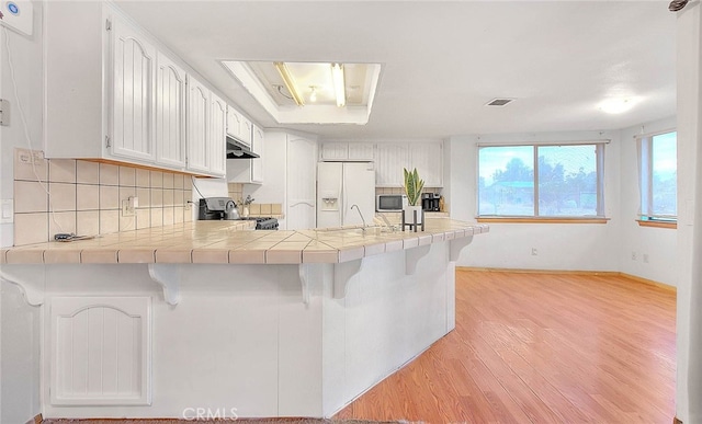 kitchen with white fridge with ice dispenser, white cabinets, stove, and kitchen peninsula