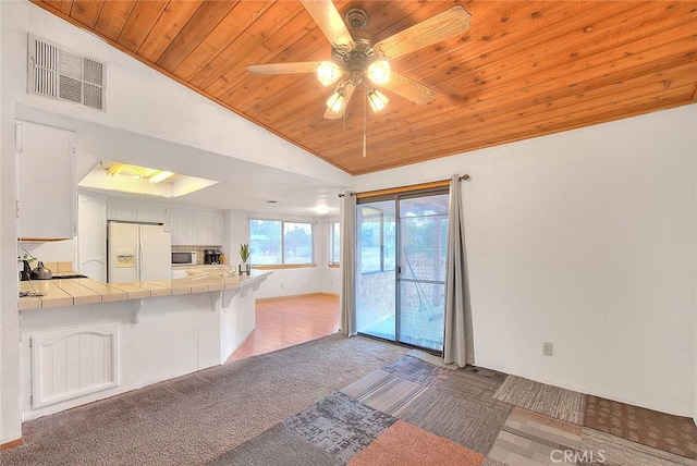 kitchen with white cabinets, lofted ceiling, carpet flooring, tile counters, and white refrigerator with ice dispenser