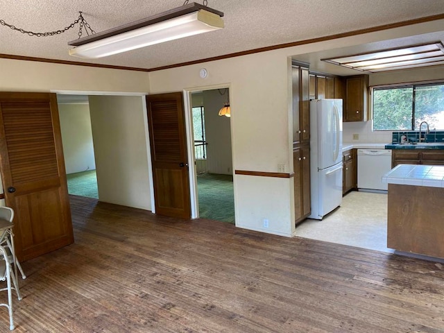 kitchen featuring white appliances, sink, tile countertops, a textured ceiling, and light hardwood / wood-style flooring