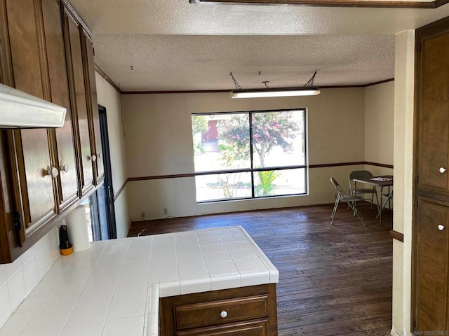 kitchen with dark wood-type flooring, tile countertops, crown molding, and a textured ceiling