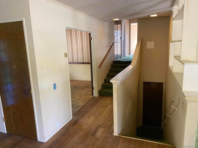 staircase with a textured ceiling, wood-type flooring, and ornamental molding