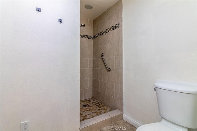 bathroom featuring toilet, tile patterned flooring, and tiled shower