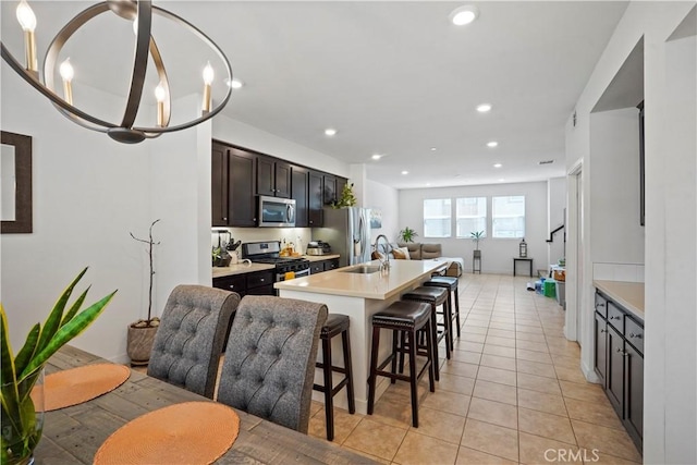 kitchen featuring appliances with stainless steel finishes, a breakfast bar, a notable chandelier, an island with sink, and light tile patterned flooring