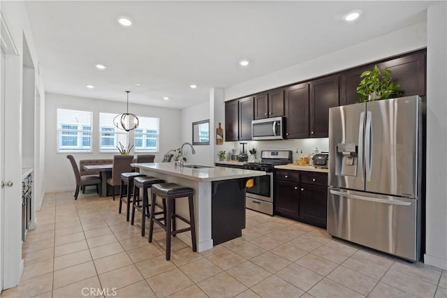 kitchen with a kitchen island with sink, hanging light fixtures, sink, a kitchen bar, and stainless steel appliances