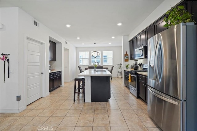 kitchen with a kitchen island with sink, sink, appliances with stainless steel finishes, decorative light fixtures, and a breakfast bar area