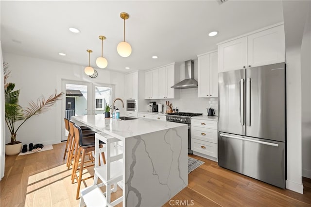 kitchen with an island with sink, wall chimney exhaust hood, white cabinetry, and stainless steel appliances