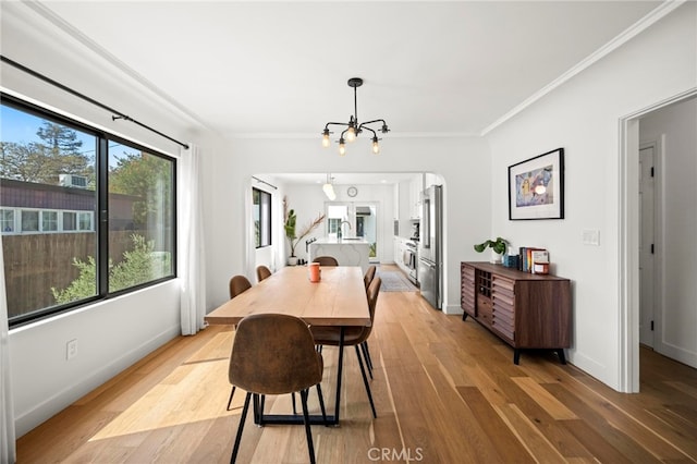 dining room with light wood-type flooring, ornamental molding, and a notable chandelier