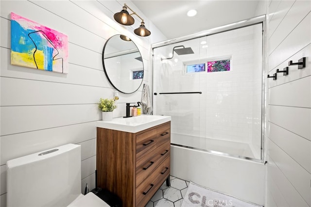 full bathroom featuring shower / bath combination with glass door, wooden walls, vanity, and toilet