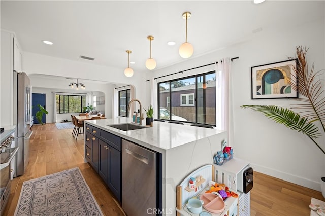 kitchen with hanging light fixtures, white cabinetry, stainless steel appliances, light hardwood / wood-style flooring, and sink