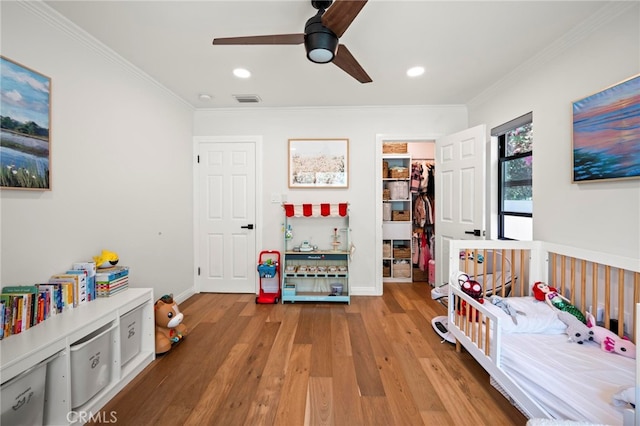 bedroom featuring light hardwood / wood-style floors, ornamental molding, ceiling fan, and a walk in closet