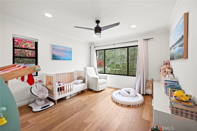 bedroom with a crib, light hardwood / wood-style floors, ornamental molding, and ceiling fan