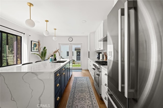 kitchen with blue cabinets, white cabinetry, pendant lighting, stainless steel appliances, and a kitchen island with sink