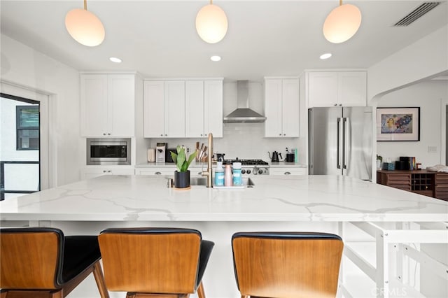 kitchen featuring stainless steel appliances, decorative light fixtures, and wall chimney range hood