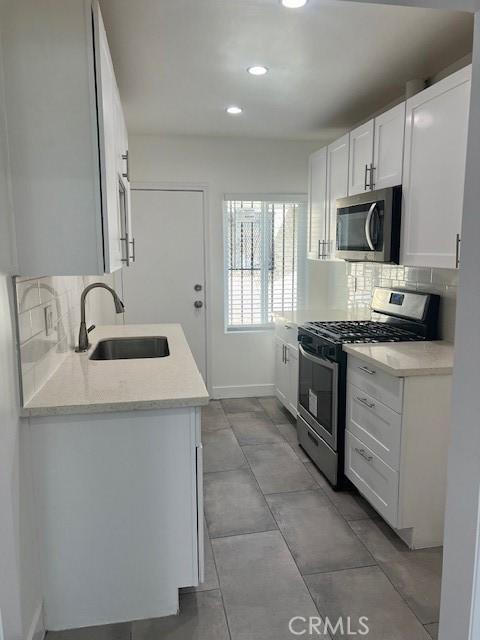 kitchen with sink, stainless steel appliances, light stone counters, decorative backsplash, and white cabinets