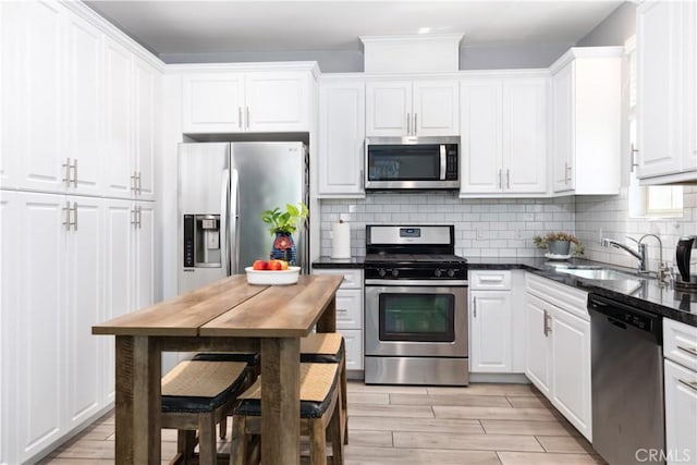 kitchen with light hardwood / wood-style floors, stainless steel appliances, backsplash, white cabinets, and sink