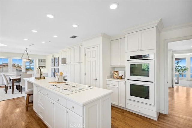 kitchen featuring white appliances, a kitchen island, pendant lighting, wood-type flooring, and white cabinetry