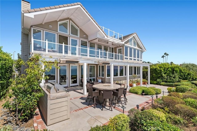 rear view of property with french doors, a balcony, and a patio area