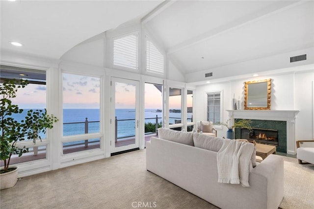 living room featuring a fireplace, beamed ceiling, a water view, and light colored carpet