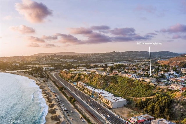 aerial view at dusk featuring a water view and a beach view