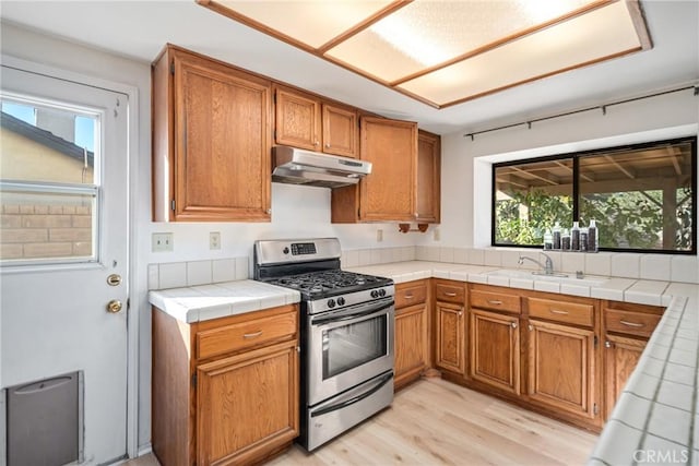 kitchen with tile counters, stainless steel gas stove, sink, and light hardwood / wood-style flooring