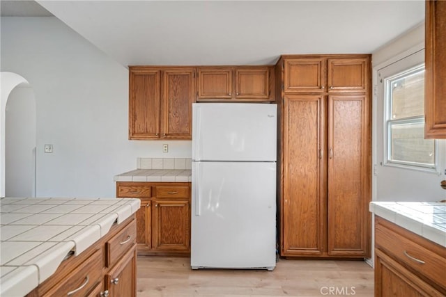 kitchen with white refrigerator, light hardwood / wood-style floors, and tile counters