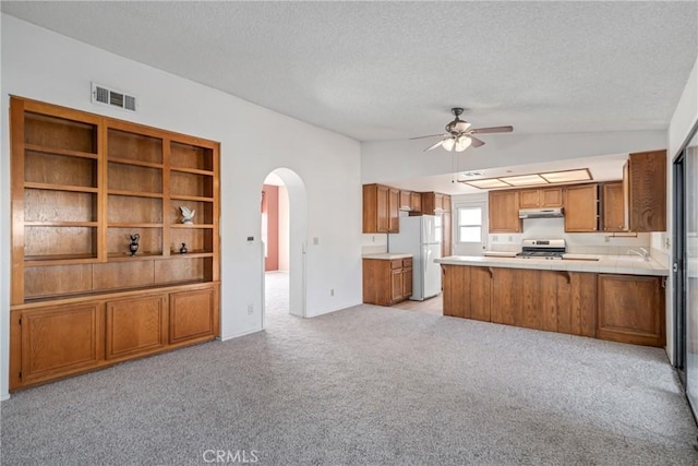 kitchen featuring light colored carpet, white refrigerator, stainless steel range oven, and kitchen peninsula