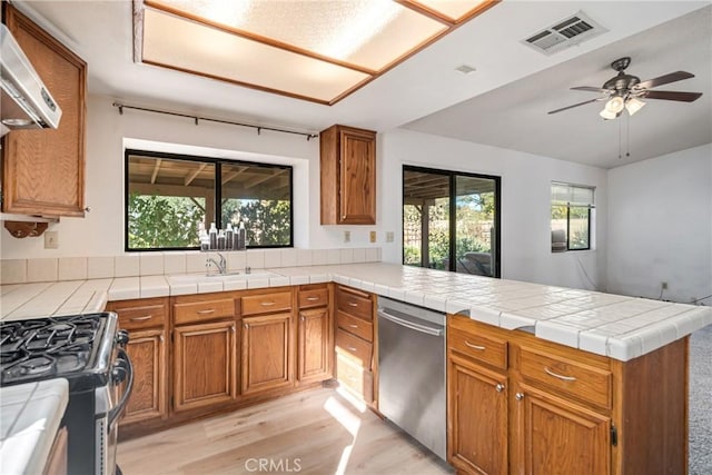 kitchen with ceiling fan, stainless steel appliances, kitchen peninsula, tile countertops, and light hardwood / wood-style floors