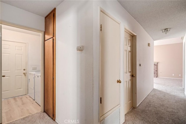 hall with light carpet, independent washer and dryer, and a textured ceiling