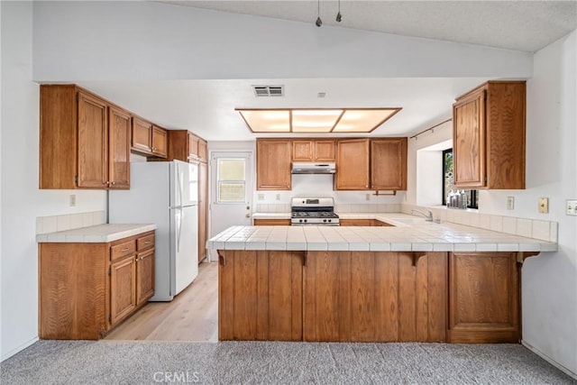 kitchen featuring tile countertops, vaulted ceiling, white fridge, kitchen peninsula, and stainless steel range with gas stovetop