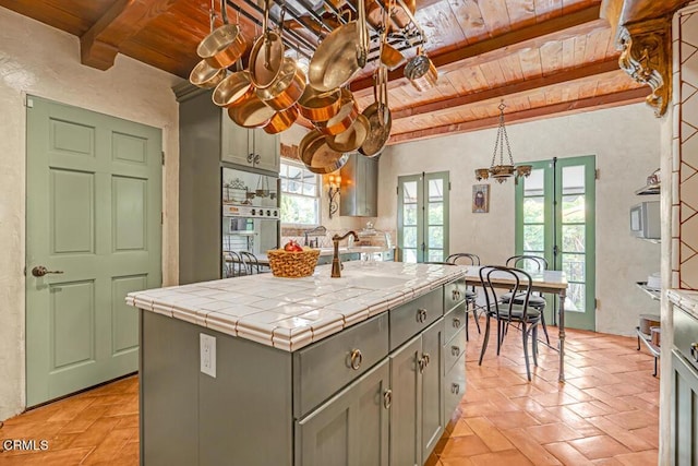 kitchen with french doors, wood ceiling, tile countertops, a center island with sink, and plenty of natural light