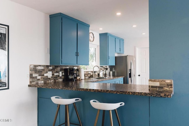 kitchen featuring decorative backsplash, kitchen peninsula, sink, blue cabinetry, and stainless steel fridge with ice dispenser