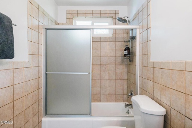 bathroom with toilet, bath / shower combo with glass door, and tile walls