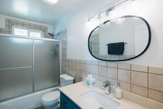 full bathroom with vanity, bath / shower combo with glass door, tile walls, and toilet