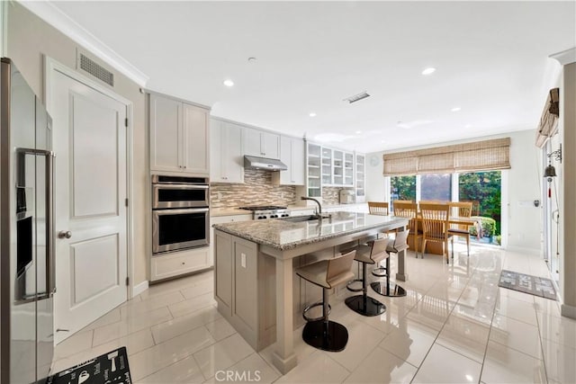 kitchen featuring a breakfast bar area, light stone counters, a center island with sink, appliances with stainless steel finishes, and white cabinets