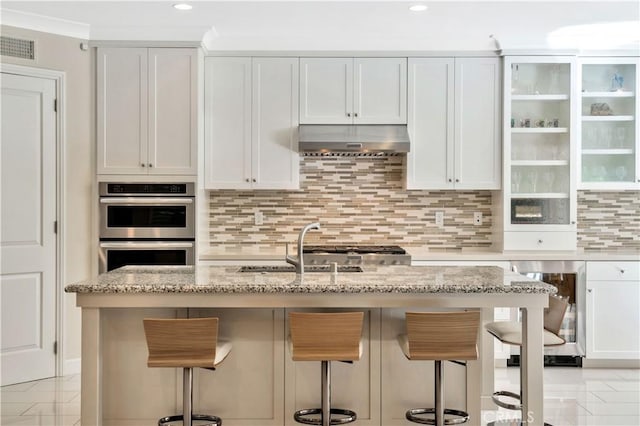 kitchen with white cabinetry, light stone counters, ventilation hood, and a breakfast bar