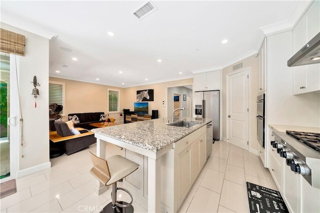 kitchen with appliances with stainless steel finishes, a breakfast bar, an island with sink, sink, and wall chimney exhaust hood